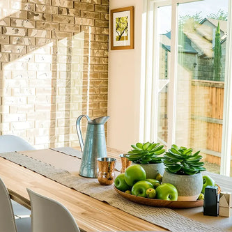 Stylish home dining area with wooden furniture, industrial pendant lighting, and natural sunlight.