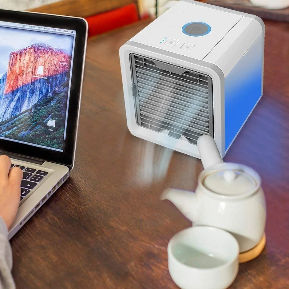 Small air conditioner on a table next to a laptop and teapot