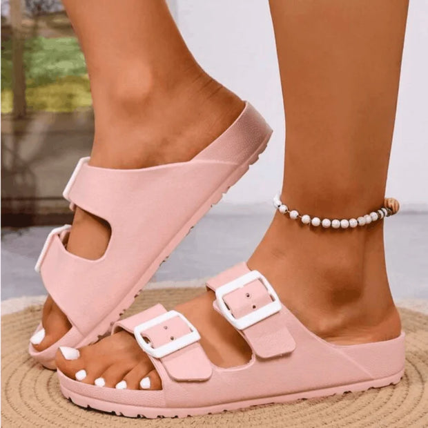 Pink sandals with white buckles worn by a person on a blurred outdoor background