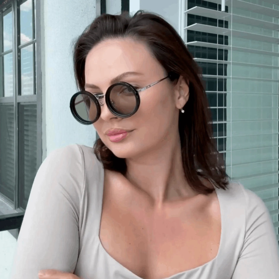 Woman wearing large round sunglasses indoors with a neutral background