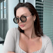 Woman wearing large round sunglasses indoors with a neutral background