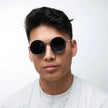 Person wearing round sunglasses and a white shirt on a light background