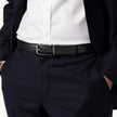 A close-up of a person wearing a black leather belt with a silver-toned rectangular buckle, styled with a white dress shirt and dark navy trousers.