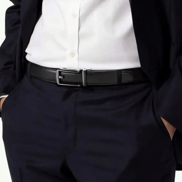 A close-up of a person wearing a black leather belt with a silver-toned rectangular buckle, styled with a white dress shirt and dark navy trousers.