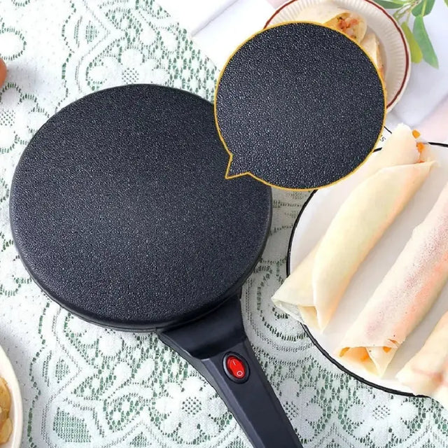Black electric crepe maker on a table with rolled-up crepes.