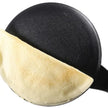 Black frying pan with a partially cooked pancake on a white background