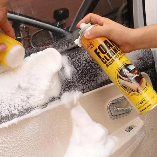 Person cleaning a car interior with a foam cleaner spray and sponge.