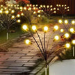 Decorative outdoor lights on a pathway with plants and a wooden fence in the background