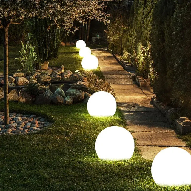 Glowing spherical garden lights along a pathway in a garden setting.