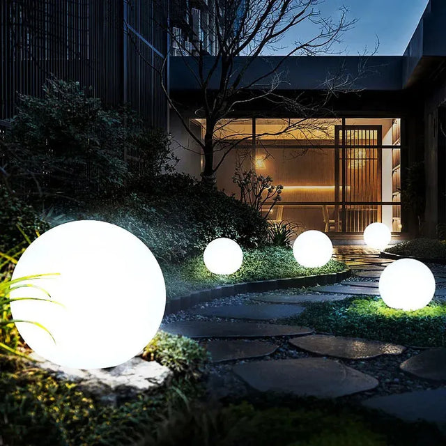 Glowing spherical outdoor lights in a garden setting with a modern house in the background.