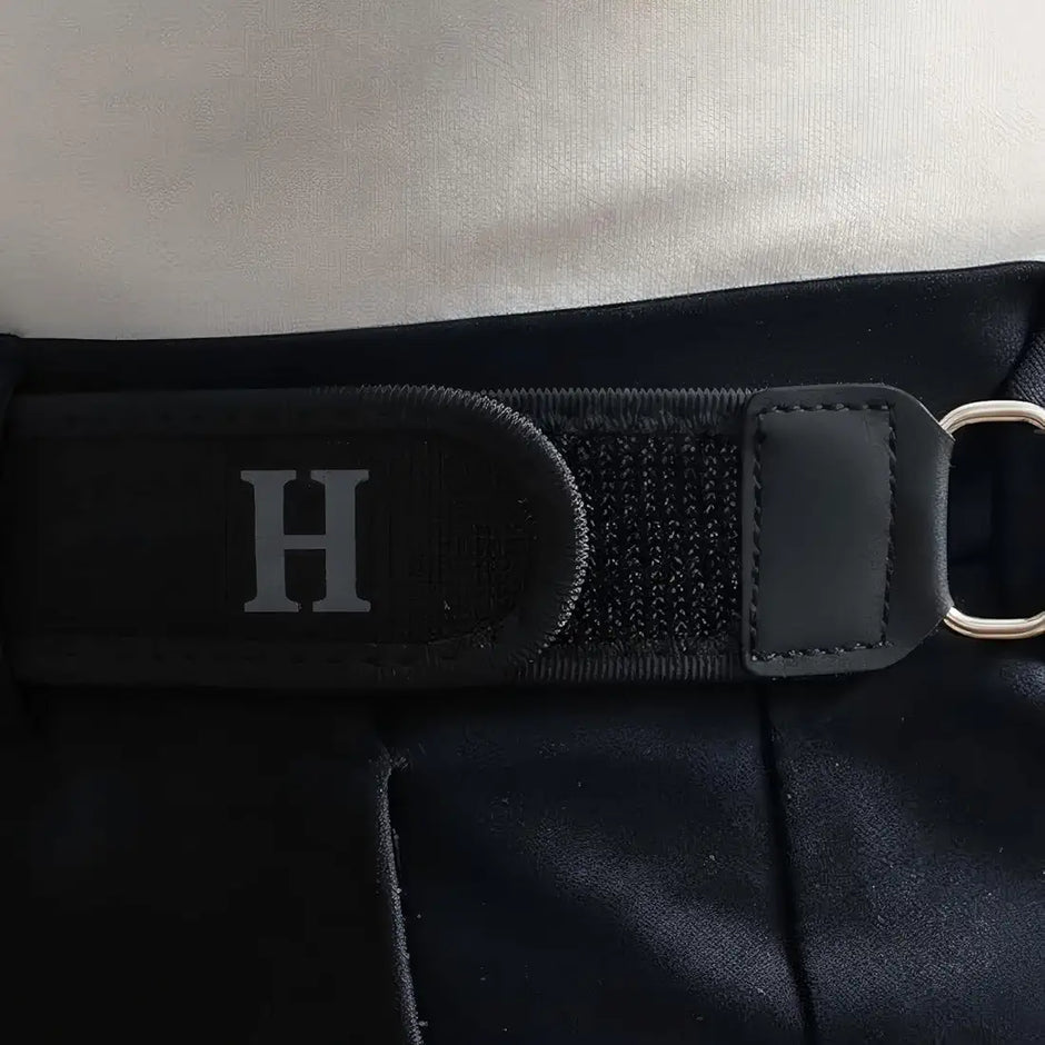 Close-up of a black strap with a silver 'H' on a textured surface