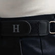 Close-up of a black strap with a silver 'H' on a textured surface