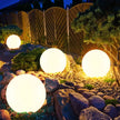 Glowing spherical outdoor lights on a stone path with a wooden fence and plants in the background.