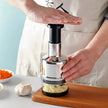 Person using a garlic press on a wooden cutting board with ingredients in the background.