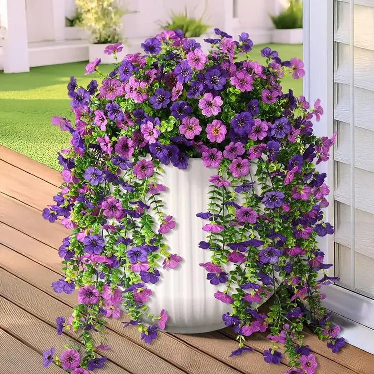 Artificial flower arch with purple and pink flowers on a wooden deck.