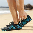 Person wearing black and blue patterned shoes on a beach.