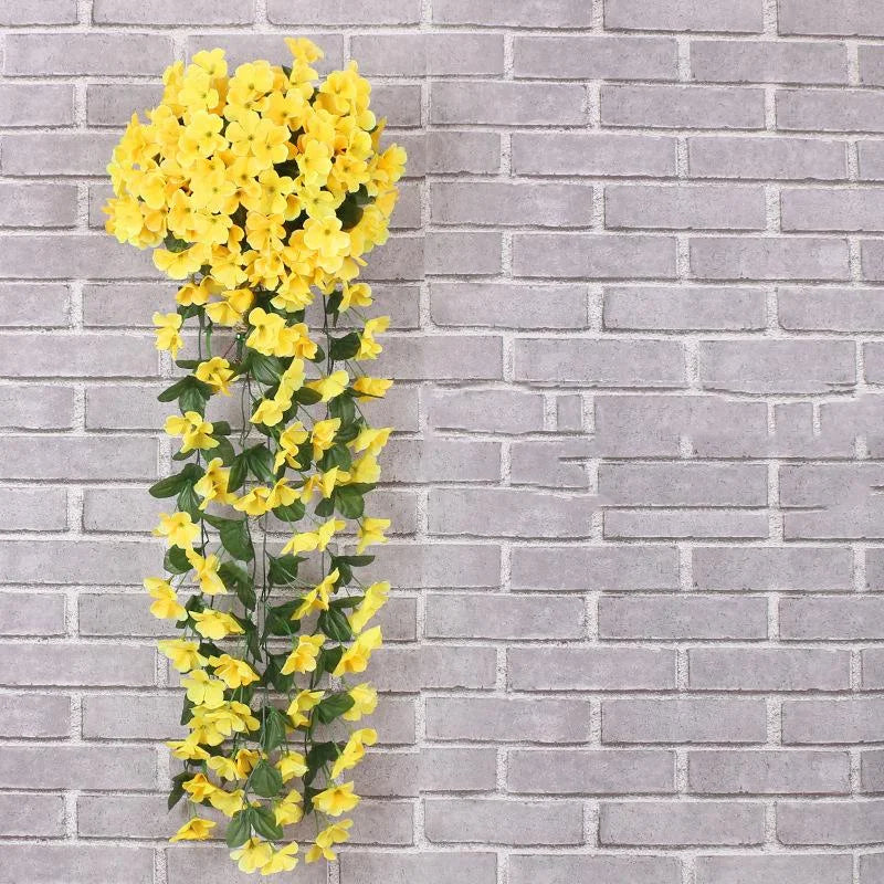 Artificial yellow flowers on a metal stand against a gray brick wall