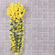 Artificial yellow flowers on a metal stand against a gray brick wall