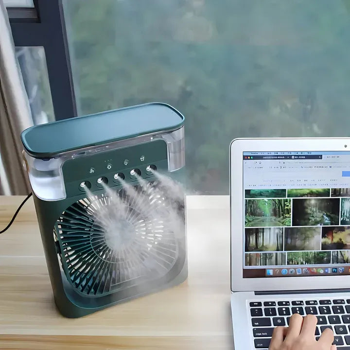 Portable air cooler on a desk next to a laptop with a forest-themed screen
