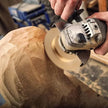 Person using a power tool on a wooden object in a workshop setting