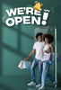 Two people standing in front of a glass door with shopping bags, and text 'We're Open!' on a green background.