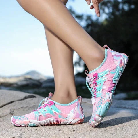 Pink and blue water shoes worn by a person on a rocky surface with a blurred natural background