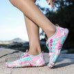 Pink and blue water shoes worn by a person on a rocky surface with a blurred natural background