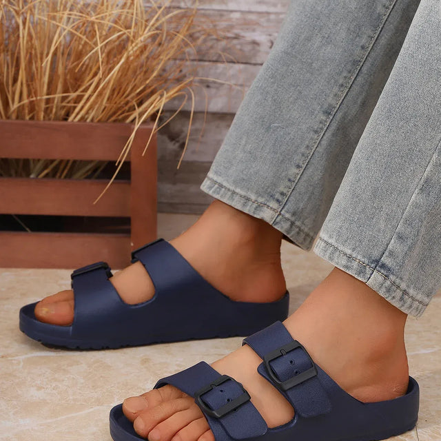 Navy sandals worn with light jeans on a wooden floor.