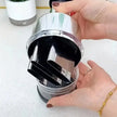 Person holding a metallic kitchen tool with black interior on a white surface