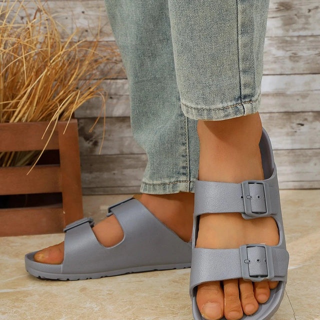 Person wearing gray sandals on a wooden floor with a plant in the background