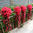 Artificial pink flowers arranged on a metal railing against a gray wall.