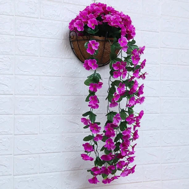 Artificial purple flower vine hanging from a wooden basket against a white brick wall.