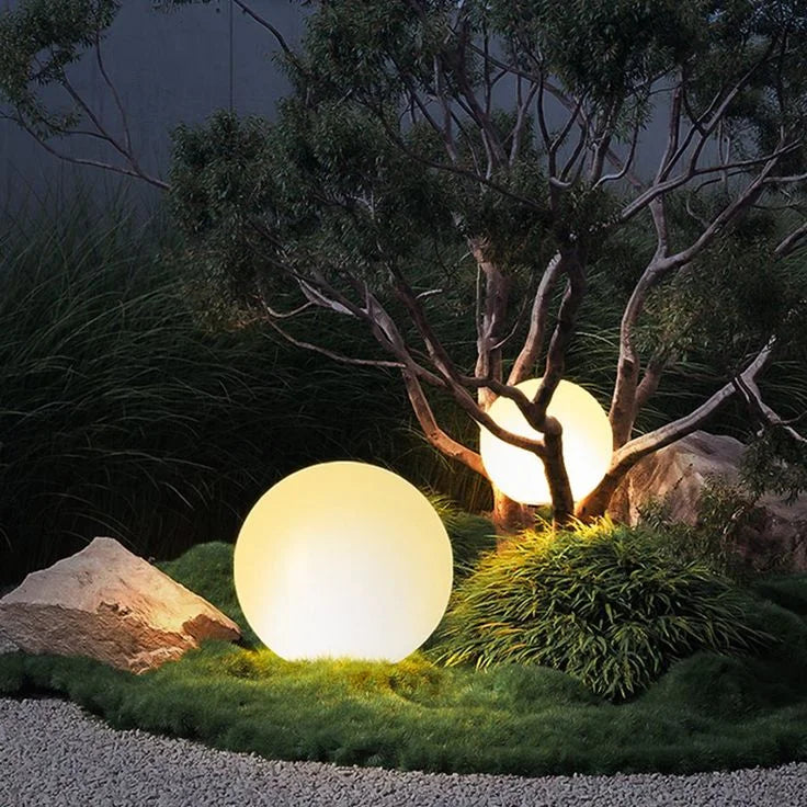 Glowing spherical outdoor lights in a natural setting with trees and rocks.