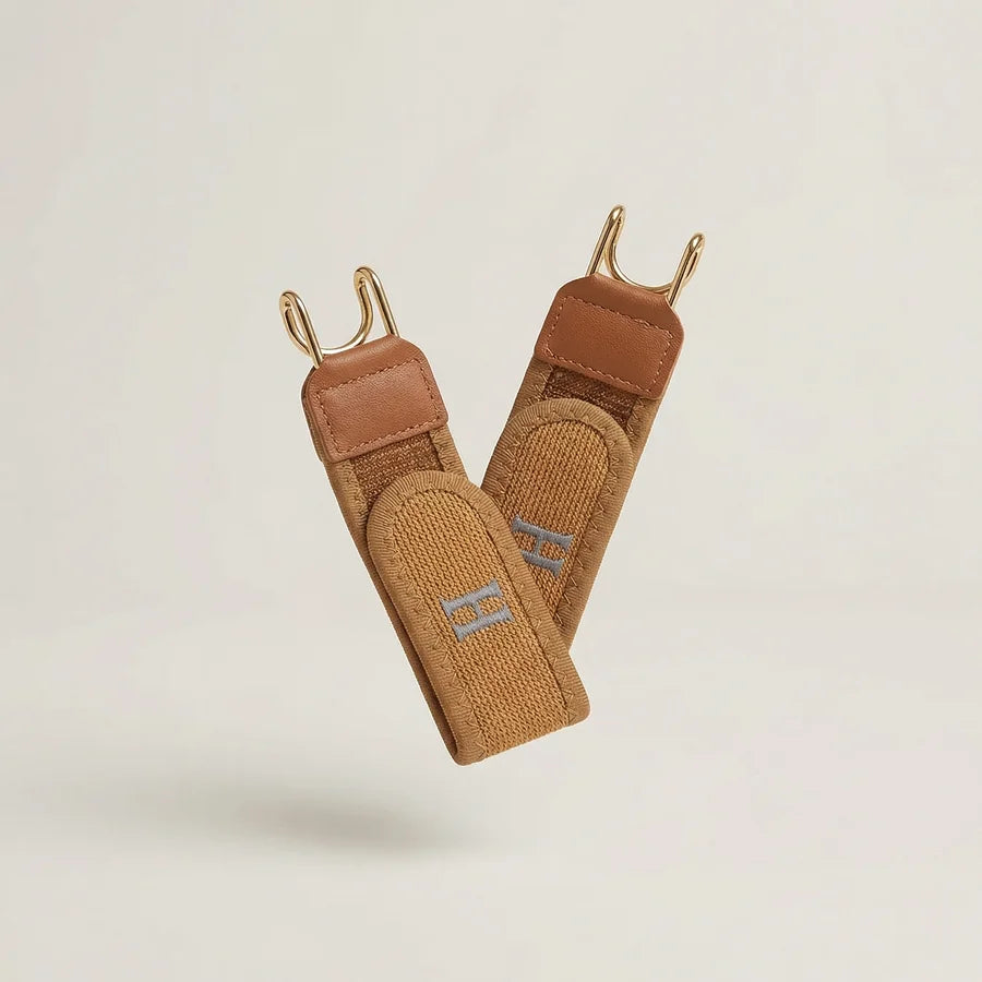Pair of brown leather straps with gold hooks on a light beige background