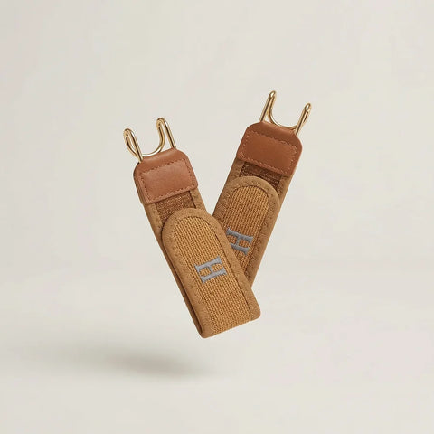 Pair of brown leather straps with gold hooks on a light beige background