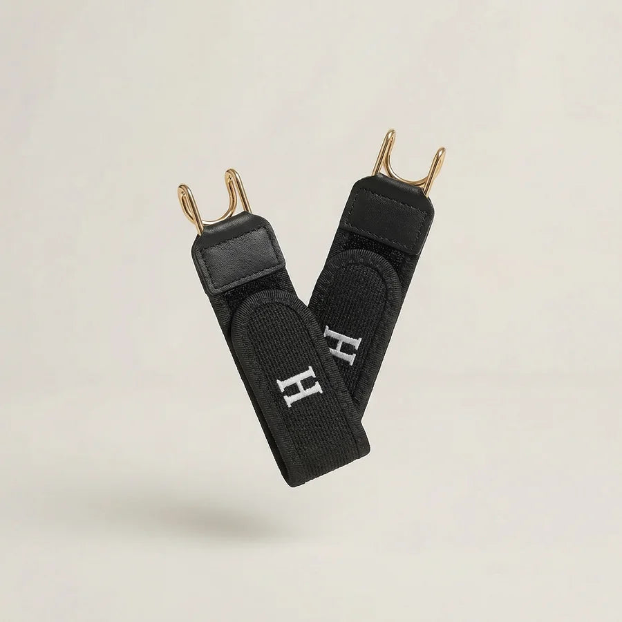 Black straps with gold hooks and a visible logo on a light beige background