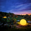 Glowing spherical light in a garden at night with a colorful sky.