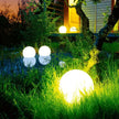 Glowing spherical outdoor lights in a garden setting with a house in the background.