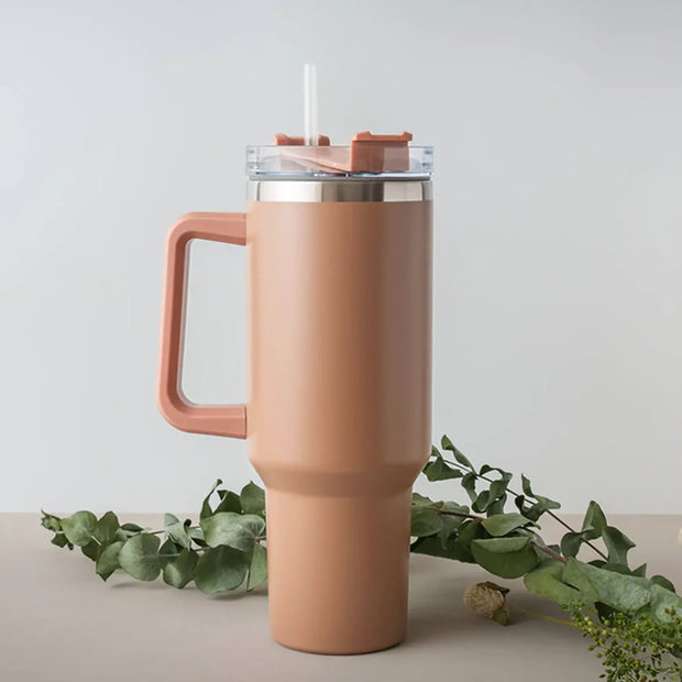 Pink insulated tumbler with handle on a light gray background with green leaves.