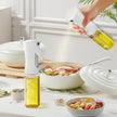 Person using an olive oil sprayer over a salad on a kitchen counter.