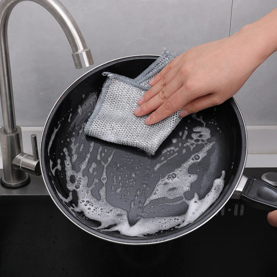 Person cleaning a frying pan with a sponge in a kitchen setting