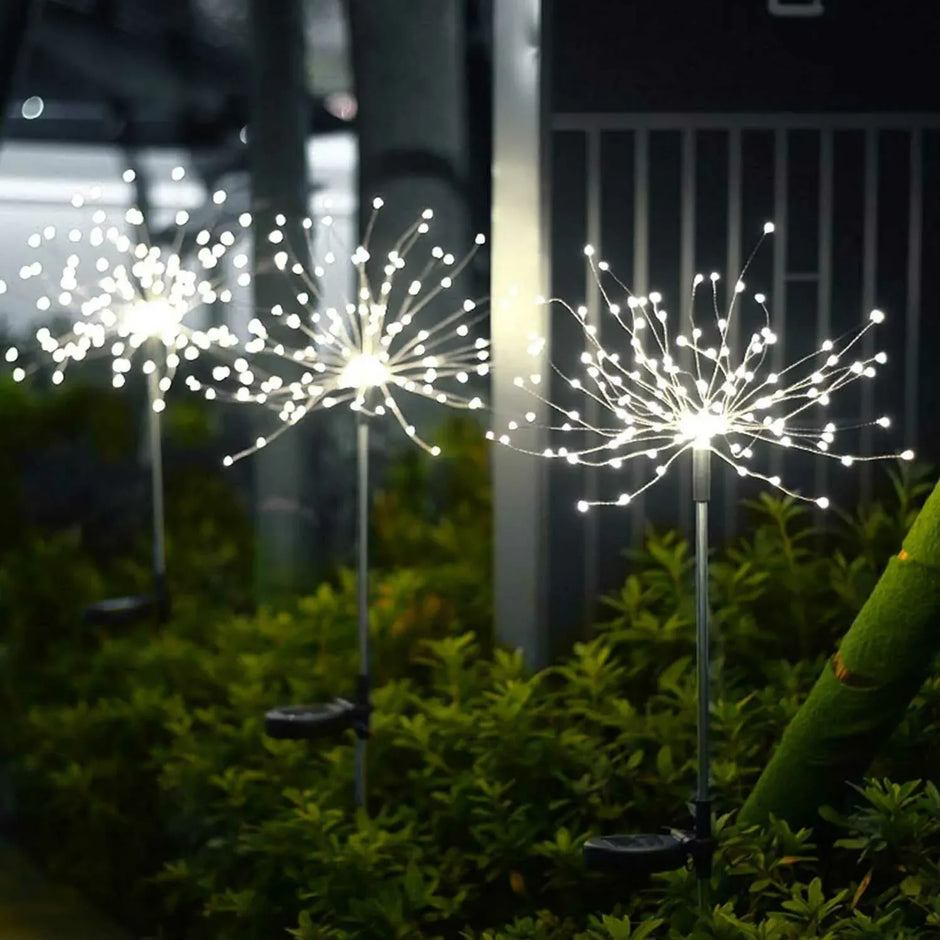 Decorative outdoor lights resembling fireworks on a grassy area at night.