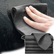 Gray microfiber cloth being used to clean a car window with a hand, and a stack of similar cloths below.
