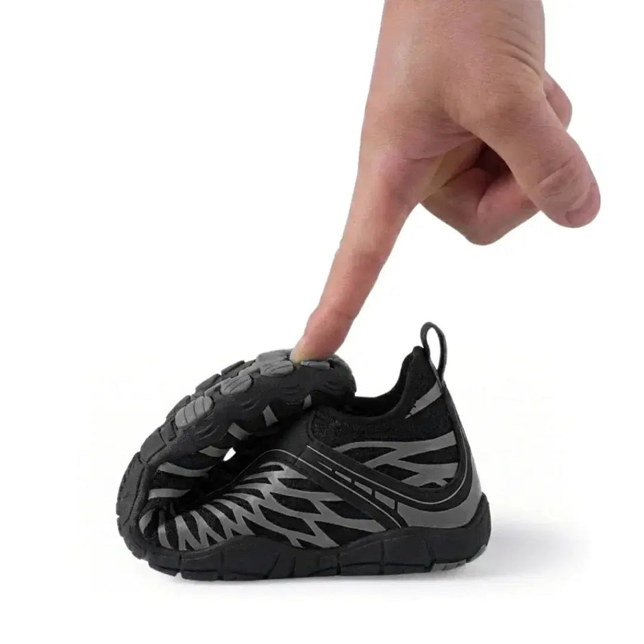 Small black and gray sneaker being pointed to by a finger on a white background
