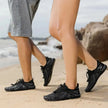 Two people wearing black water shoes on a beach.