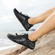 Black water shoes worn by a person on a beach