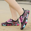 Black, pink, and blue water shoes on a sandy surface