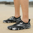 Black and white water shoes on feet standing on sand with blurred background