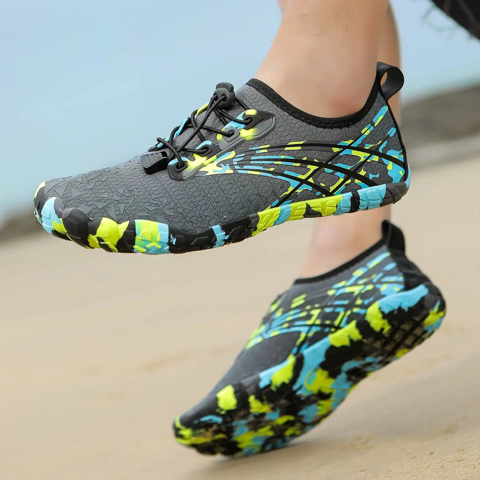 Colorful water shoes with black, blue, and green pattern worn on a sandy surface.