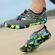Colorful water shoes with black, blue, and green pattern worn on a sandy surface.